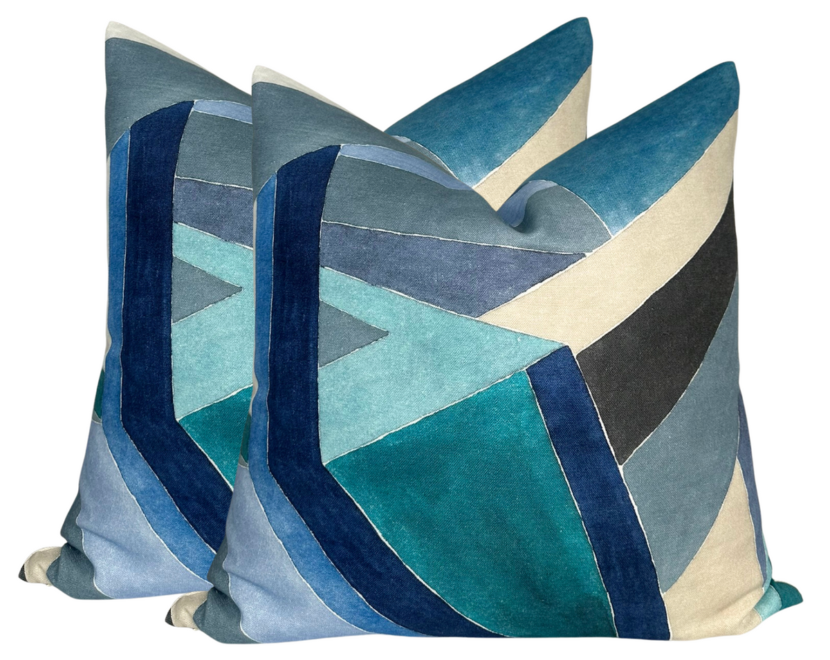 Two square pillow covers with a geometric pattern of overlapping blue, teal, cream, and gray velvet shapes creating a layered chevron design.