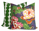 Two square pillows with Schumacher textiles: front pillow has green background with large multicolored floral and leaf patterns, back pillow features vertical green scalloped stripes on white.