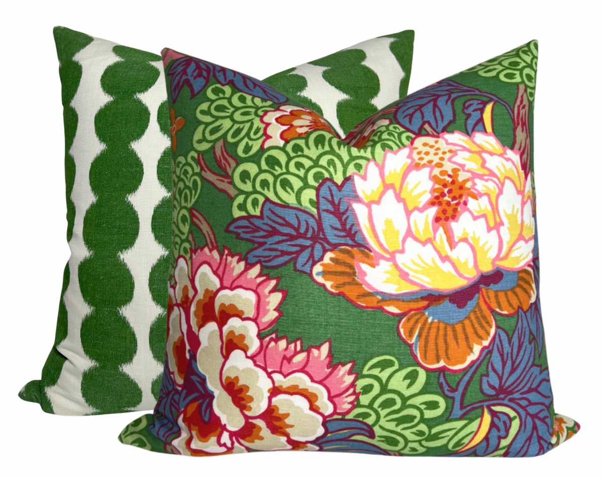 Two square pillows with Schumacher textiles: front pillow has green background with large multicolored floral and leaf patterns, back pillow features vertical green scalloped stripes on white.
