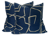 Two square indigo pillow covers with abstract beige linear patterns creating an angular, modern design, shown angled side by side on a white background.