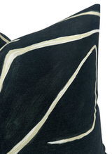 Close-up of a black pillow cover with abstract beige brushstroke lines forming angular shapes, highlighting a textured fabric surface.
