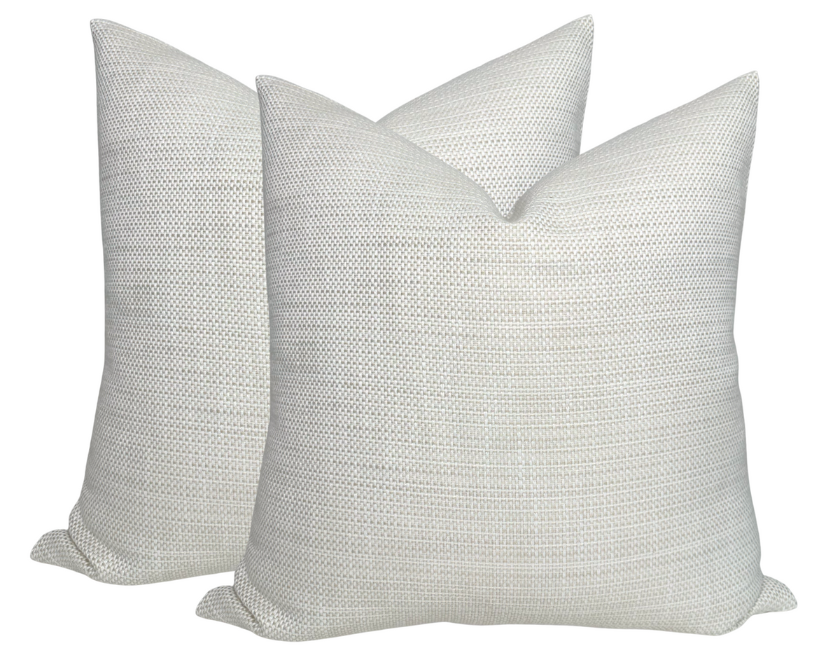 Two tan-colored woven fabric pillow covers with subtle horizontal texture and pointed corners, arranged overlapping on a white background.