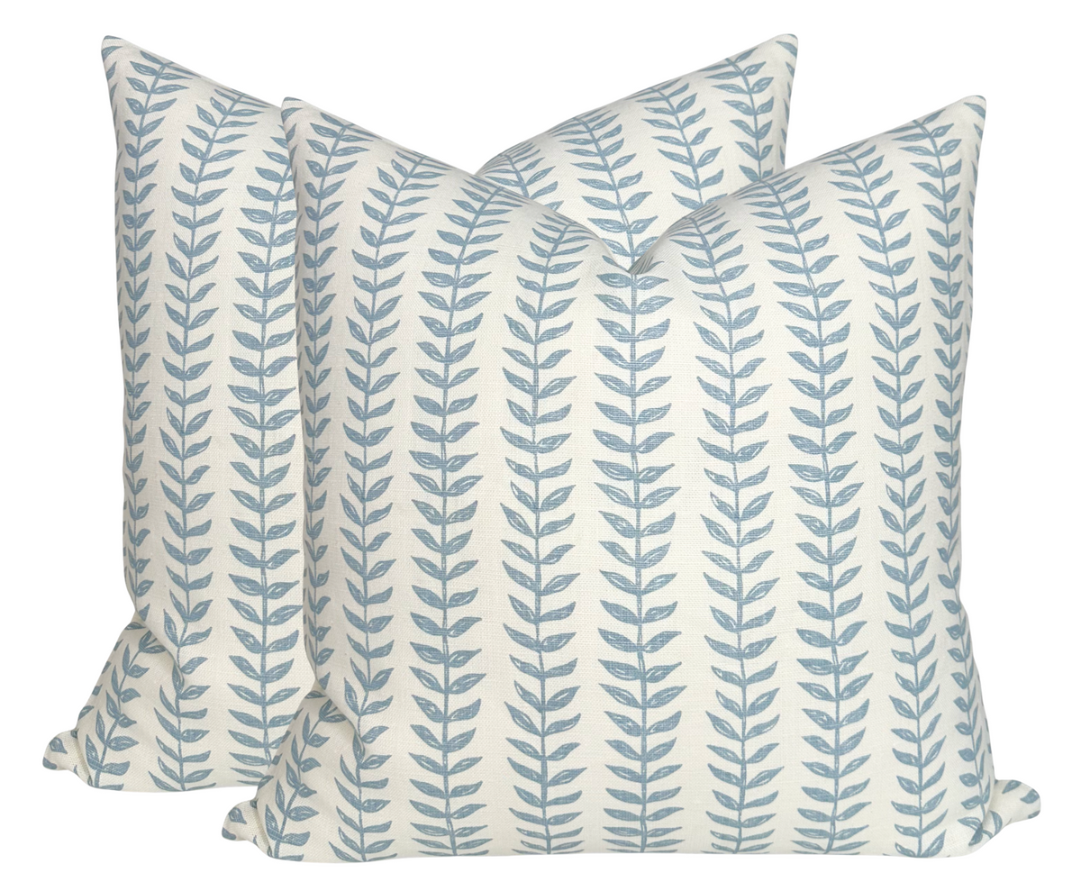 Pair of square linen pillow covers with repeating vertical blue willow leaf patterns on an off-white background, arranged slightly overlapping.