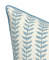 Close-up of a linen pillow cover featuring blue vertical willow branch patterns on off-white fabric with matching blue piping along the edges.