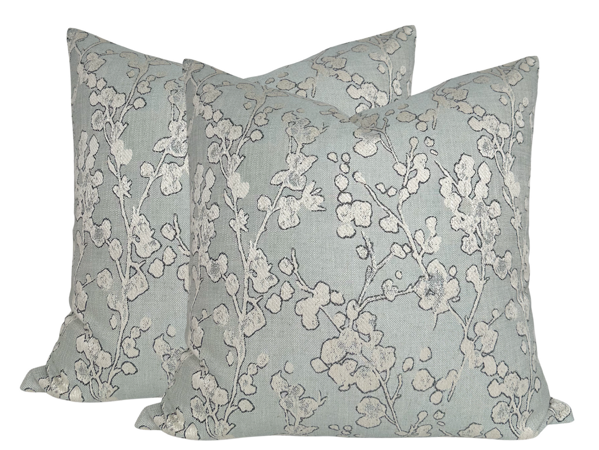 Pair of square pillows with eucalyptus green background and off-white floral branches embroidery, showing soft texture and subtle color contrast.