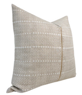Square pillow cover in sand brown with horizontal stripes of small repeated geometric motifs in white, showing a slight fold at the bottom corner.