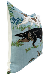 Rectangular pillow with sky blue background featuring illustrations of a black and white pointer dog among grass and plants, edged with off-white fabric sides.