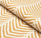 Close-up of cream fabric with a repeating abstract marigold chevron pattern, showing texture and slight folds in the material.