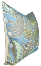 Square pillow with spa blue front featuring intricate botanical patterns in beige, white, and green, and a plain cream-colored back panel, shown at an angle.