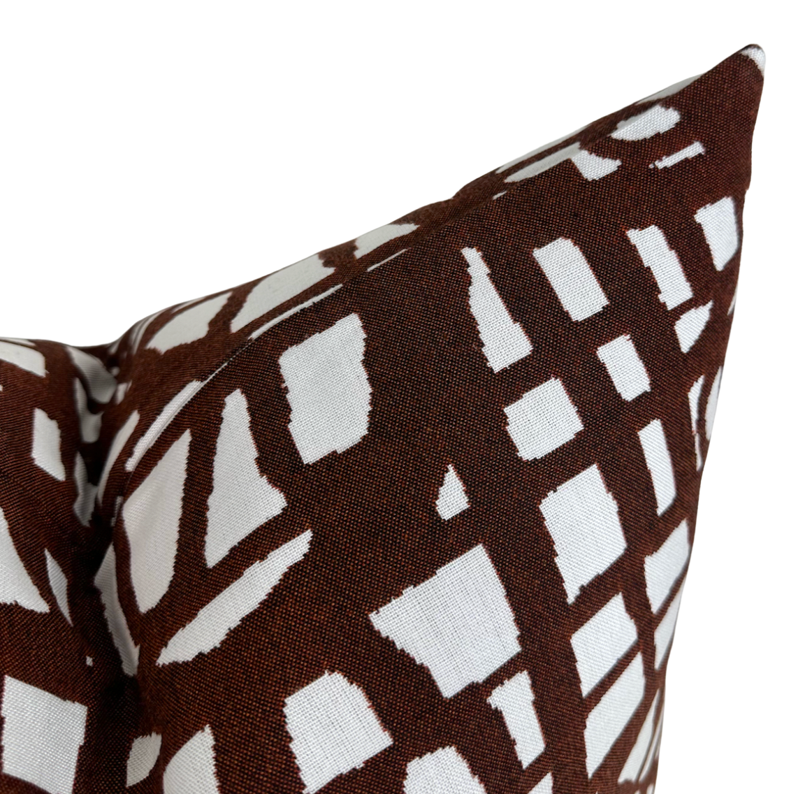 Close-up of a rust-colored pillow cover with an abstract grid pattern in white, made of textured fabric and shown from an angled top view.