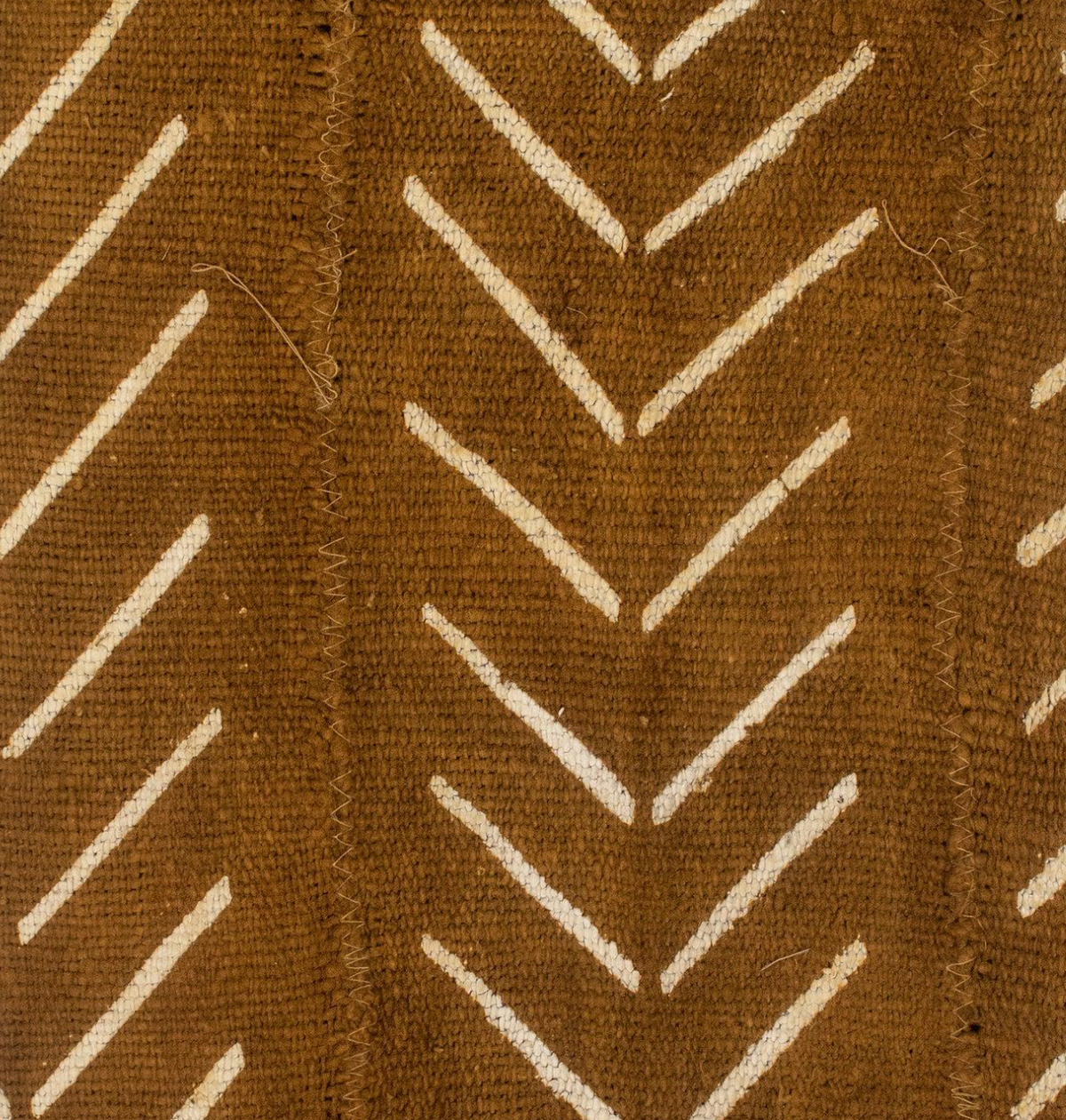 Close-up of brown mudcloth fabric with white chevron pattern arranged in vertical stripes, showing stitching details of the textile.
