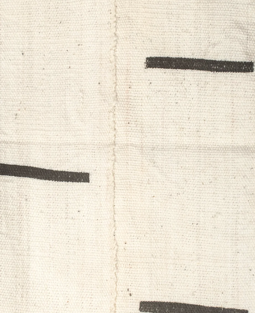 Close-up of ivory mudcloth fabric with simple black horizontal dash pattern and visible coarse weaving texture along the central seam.