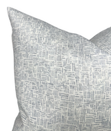Close-up of a dove grey pillow cover with an irregular geometric pattern of short, intersecting lines creating a woven effect on a white background.