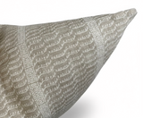 Close-up of a pillow corner featuring a woven beige and off-white pattern with vertical textured stripes and abstract leaf motifs on a soft fabric.
