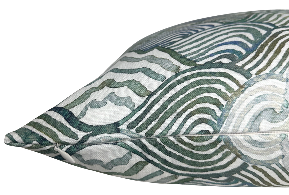 Close-up of a pillow cover featuring overlapping circular and wavy line patterns in shades of green and blue on a white fabric background.