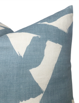 Close-up of a linen pillow cover in sky blue with bold, irregular white brushstroke patterns creating an abstract design.