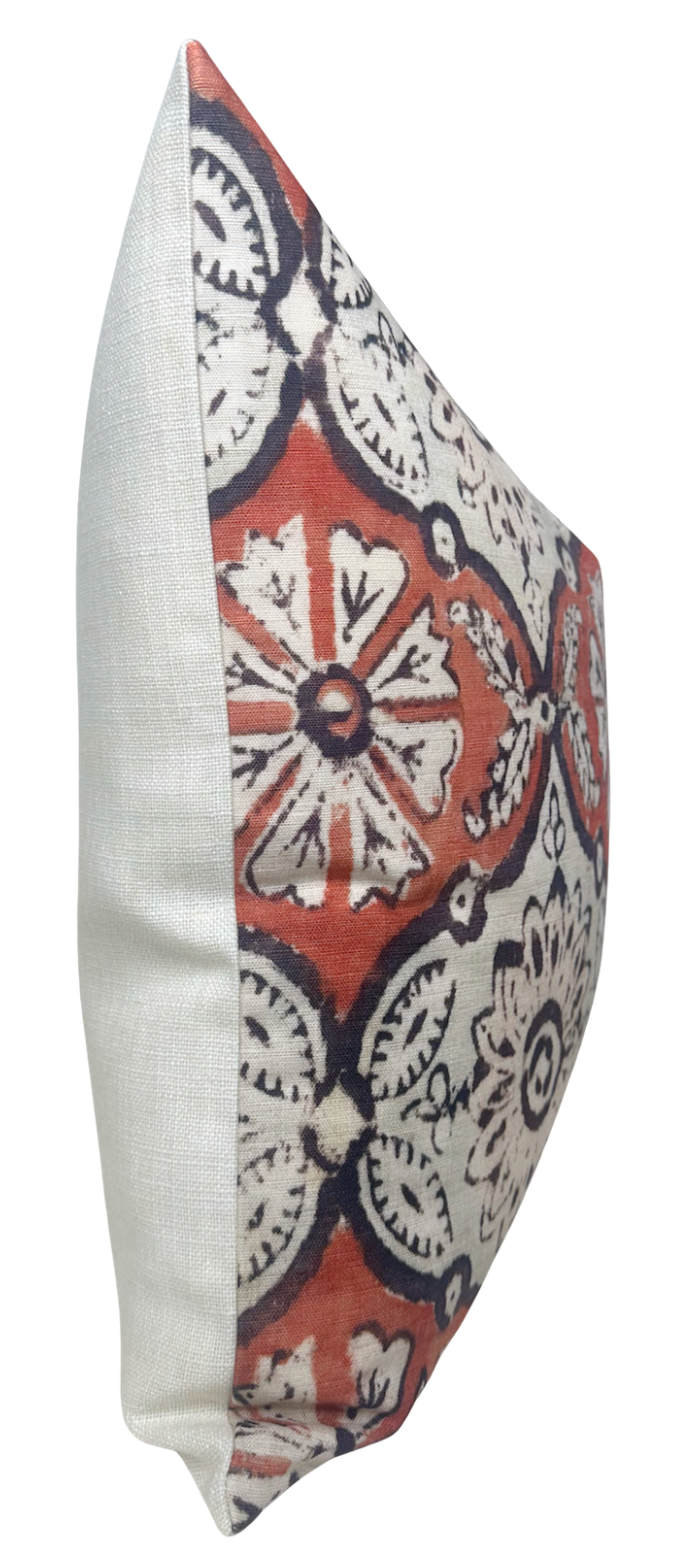 Square pillow with a bold ruby red background featuring white and black floral and circular patterns, contrasted by a plain off-white fabric on the side.