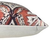 Close-up of a pillow corner featuring a muted red and black floral pattern on textured fabric with a white back and a small white zipper.