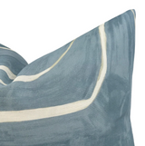 Corner of a 20x20 pillow cover in muted sky blue with white and tan abstract linear patterns resembling brush strokes