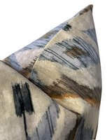 Close-up of two soft velvet pillow corners with abstract brushstroke patterns in muted blue, beige, brown, and black hues.