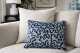 Rectangular pillow with blue textured abstract pattern on a light background, placed against a plain light-colored square pillow on a textured beige sofa.