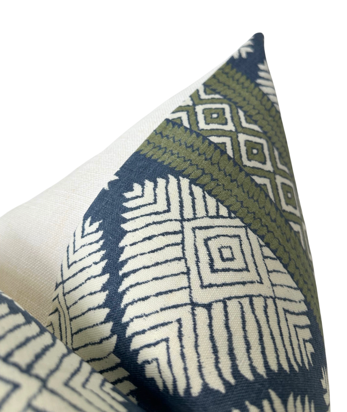 Close-up of pillow corner with geometric patterns in bluestone blue, olive green, and off-white on fabric.