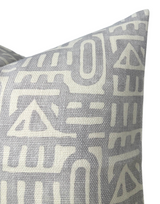 Close-up of a gray pillow cover featuring an off-white abstract geometric pattern with triangle and linear shapes on a textured fabric.