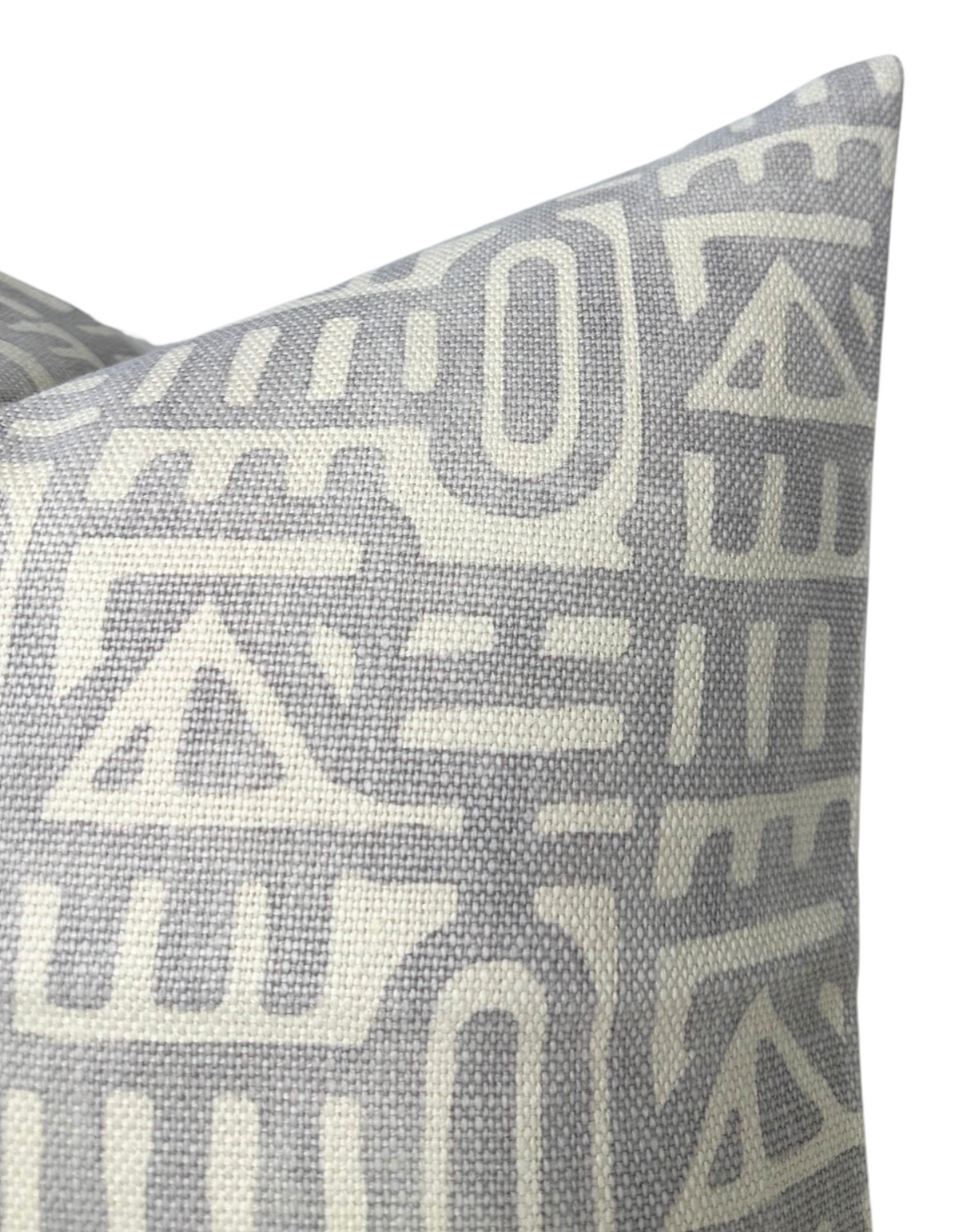 Close-up of a gray pillow cover featuring an off-white abstract geometric pattern with triangle and linear shapes on a textured fabric.
