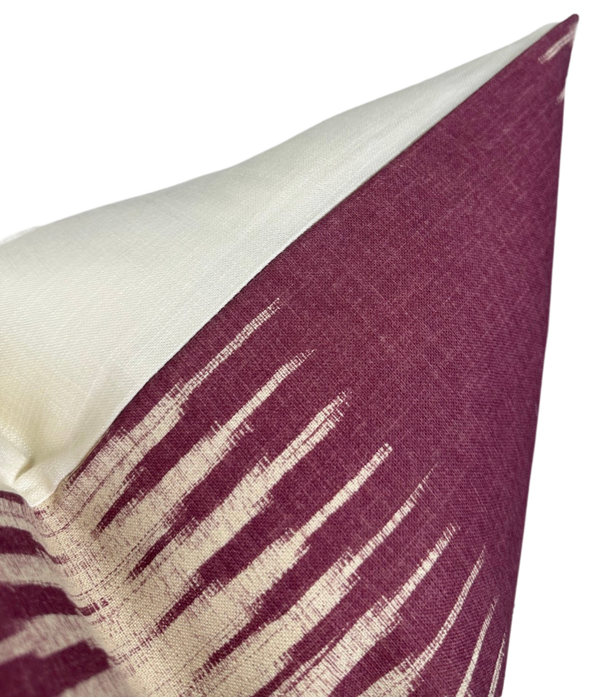 Close-up of an ikat pillow cover showing a diagonal split with creamy off-white fabric on one side and reddish-purple fabric featuring an elongated white pattern on the other.