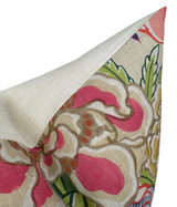 Beige pillow cover showing corner folded to reveal floral pattern in pink, green, and yellow with bold, painterly leaves and petals.