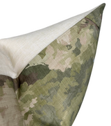 Close-up of a pillow corner showing a woodland camouflage pattern in various green and beige shades with natural linen-colored fabric on the reverse side.