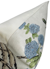 Corner detail of a beige pillow cover featuring embroidered blue pom-pom flowers with green leaves on textured fabric.
