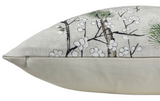 Close-up side view of a beige pillow cover featuring a botanical design with black branches, white blossoms, and green pine needles, including a visible zipper along the seam.