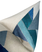 Close-up of a pillow corner with geometric patchwork in varying shades of blue and teal on a beige fabric background, highlighting texture and stitched seams.