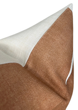 Close-up of a triangular fabric pillow cover with a warm clay brown section bordered by a narrow white edge and a contrasting off-white fabric panel.