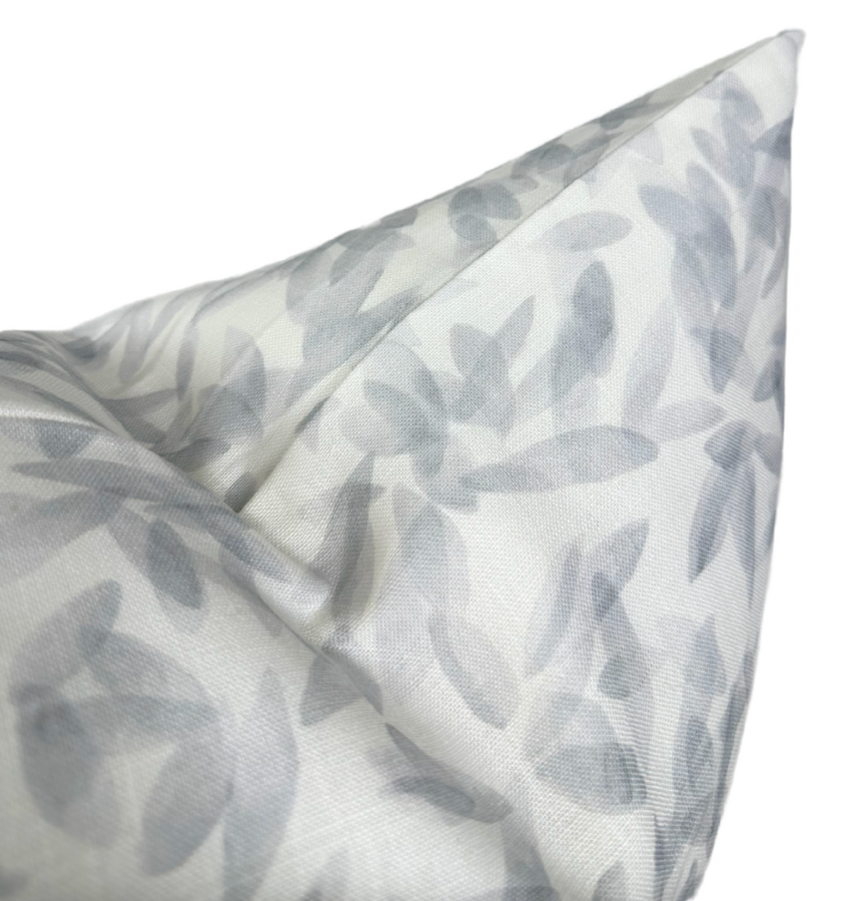 Close-up of a pillow cover with a soft gray leaf pattern on a white background, featuring a subtle, semi-transparent botanical design and a folded corner.
