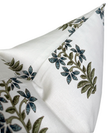 Close-up of a white pillow cover featuring green and indigo floral patterns with leafy stems, highlighting its sharp corner and fine textile texture.