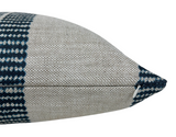 Close-up side view of a rectangular pillow with a textured beige base and indigo checkered band near the seam, featuring a small white zipper pull.
