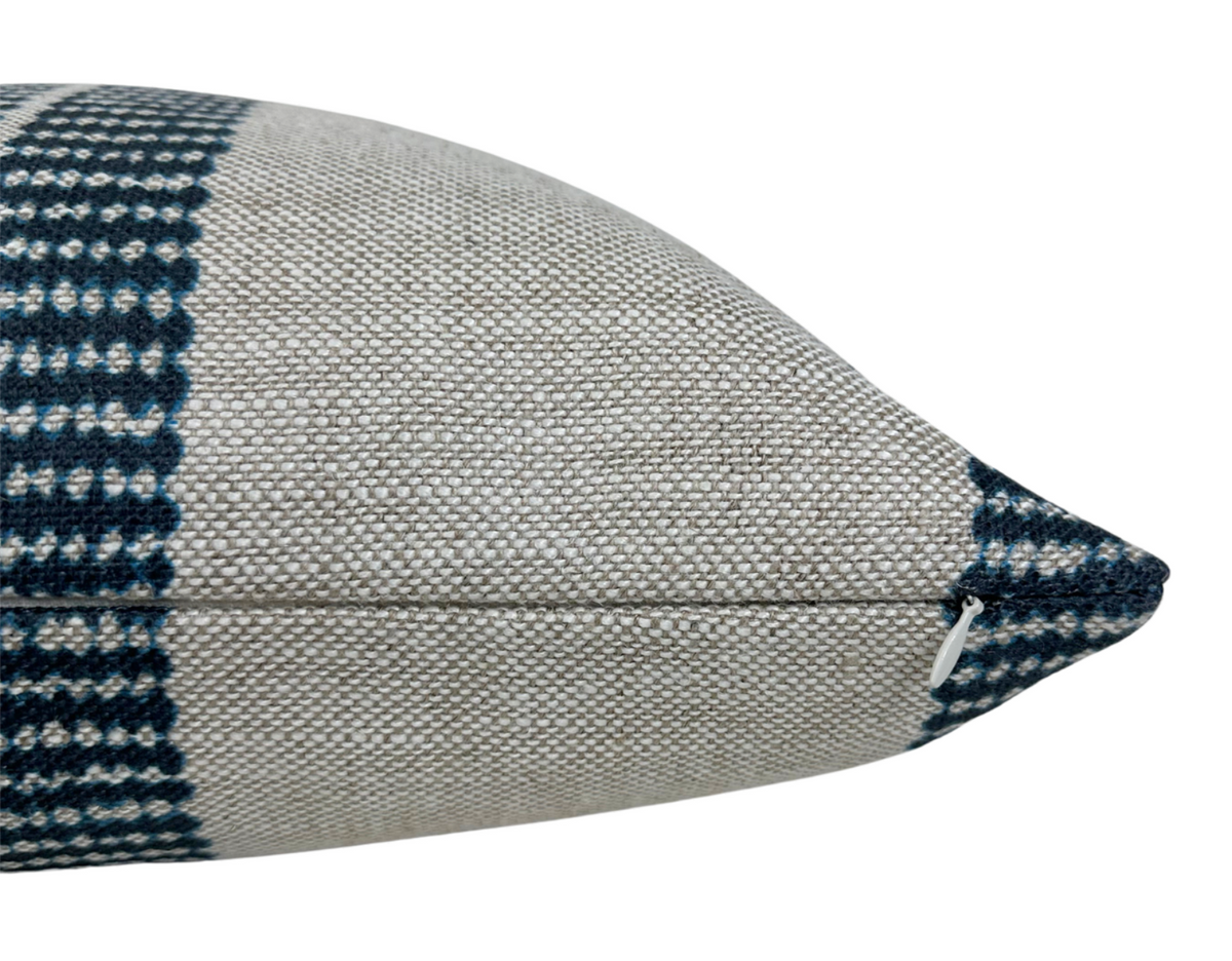 Close-up side view of a rectangular pillow with a textured beige base and indigo checkered band near the seam, featuring a small white zipper pull.