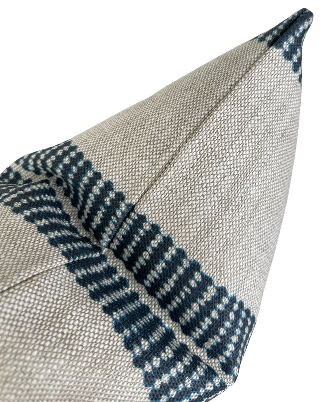 Close-up of an indigo and beige woven band pillow cover with geometric stripe patterns converging at a corner seam, showing textured fabric detail.
