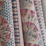 Close-up of fabric with pink and coral floral and geometric patterns, featuring blue triangles and striped details in soft, muted tones.