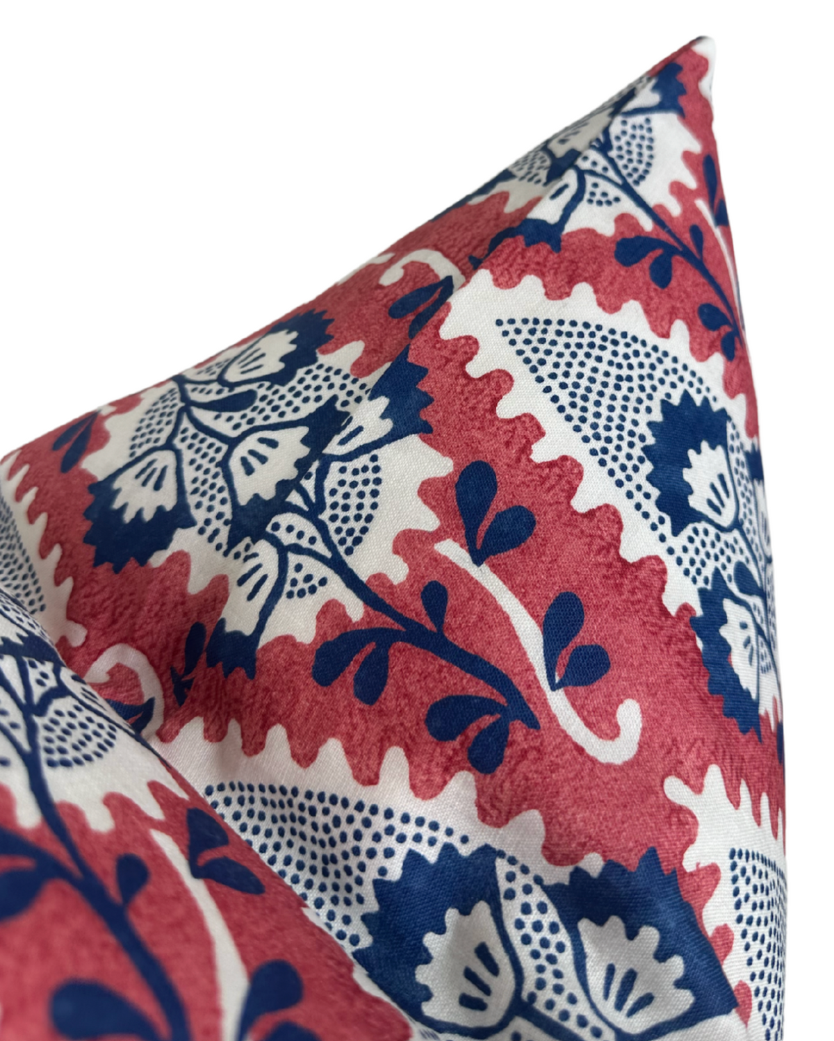 Corner of a pillow with a red scalloped background pattern featuring large navy and white floral and leaf motifs with small dot details.
