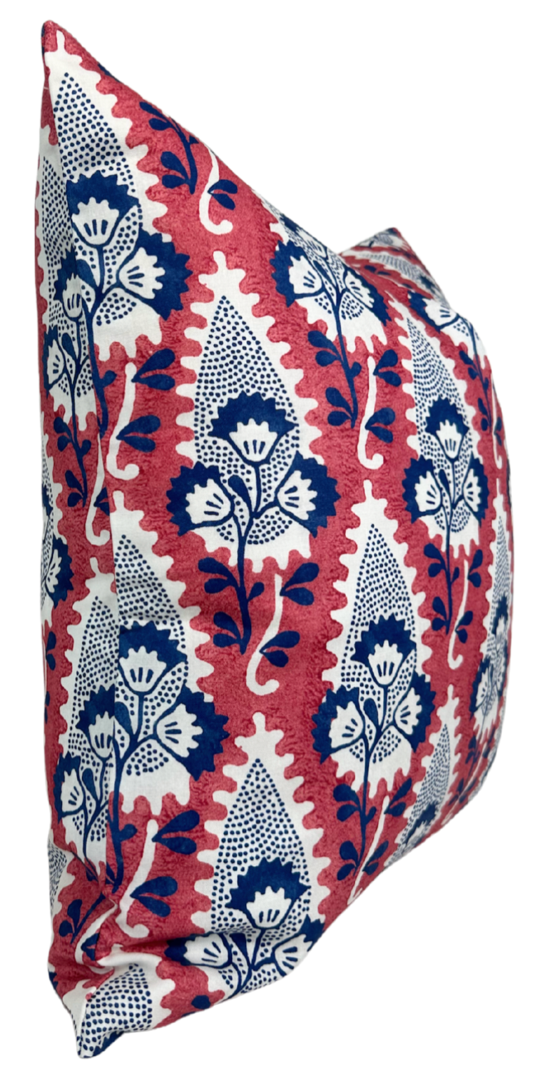 Square pillow with red background and stylized white and navy blue floral motifs in vertical rows, shown from a side angle.