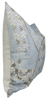 Square pillow with a sky-blue front featuring vertical white blossom branches and light beige sides, shown angled from the side.