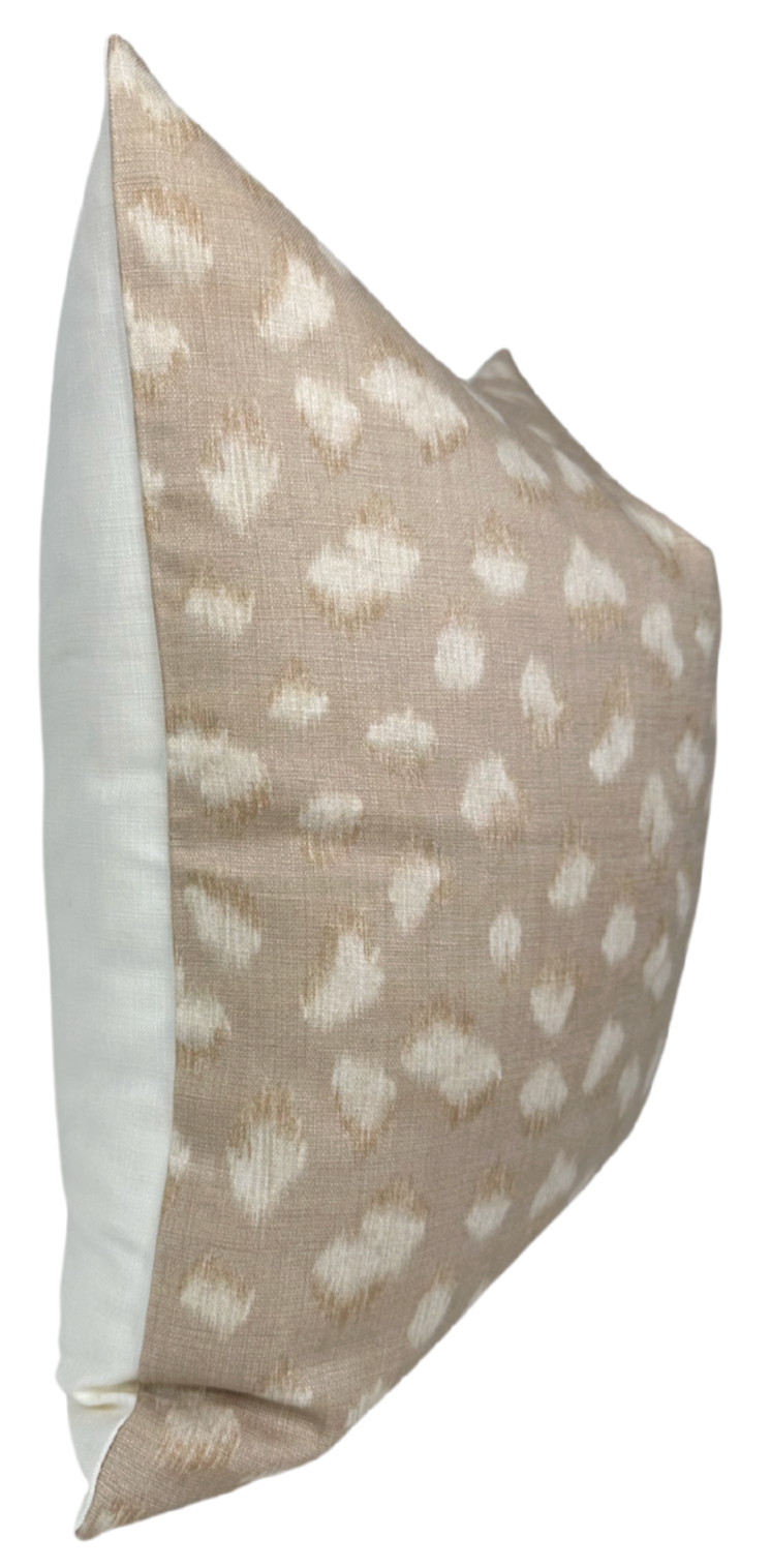 Rectangular pillow with beige front featuring an ivory abstract feline spot pattern and solid ivory back, shown from a side angle.