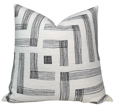Pastiche Pillow Cover in Chalk Jet resting on a dark sofa with a background of soft neutrals