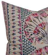 Corner of a pink and coral pillow cover featuring geometric blue triangles and floral patterns with additional linear decorative borders on beige fabric.
