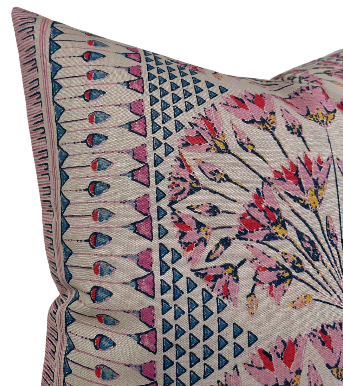 Corner of a pink and coral pillow cover featuring geometric blue triangles and floral patterns with additional linear decorative borders on beige fabric.