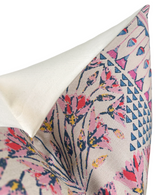 Corner of a pillow with a white reverse and a floral and geometric pattern in pink, coral, navy blue, and yellow on a light beige background.