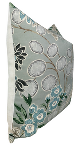 Square pillow with sage green front displaying botanical floral patterns in white, teal, black, and beige on a light cream fabric back and sides.